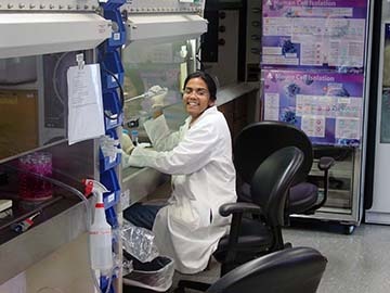 Deepani sitting in a chair in front of lab equipment smiling