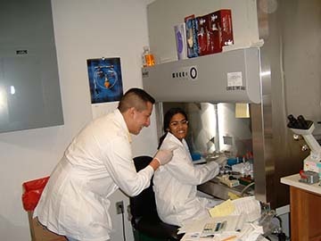 Two people in lab coats smiling and looking at equipment