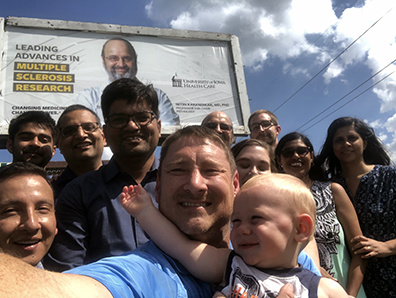 A person taking a selfie with a large group of people in front of Dr. Karandikar's billboard