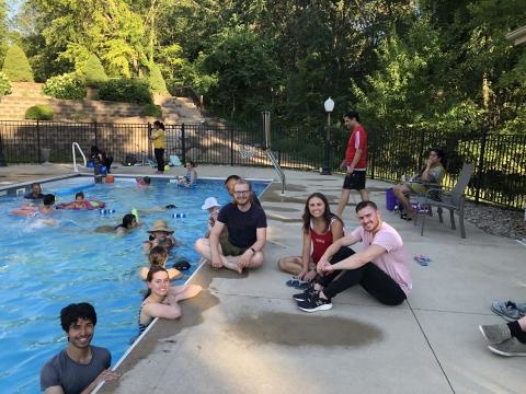 Several people in a pool near the edge and some people sitting near the edge of the pool
