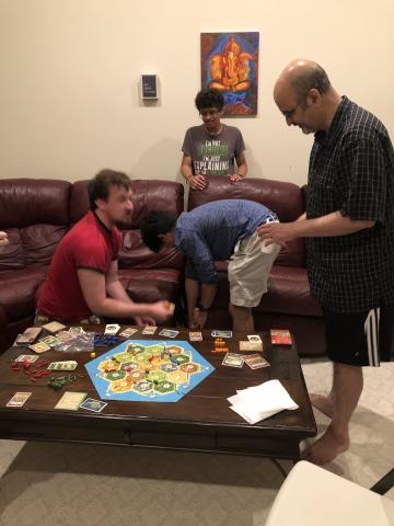 Several people looking at a Settlers of Catan game board